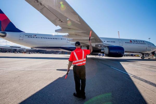 A Delta employee guides a taxiing plane.
