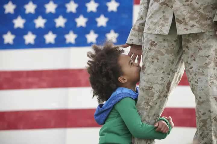 A child hugs a service member in uniform.