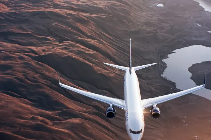 A 737-900 flies over mountains and a river.