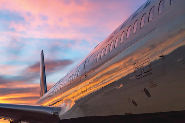 The side of a 757-200 with sunset reflected along with the tail and wing in view.