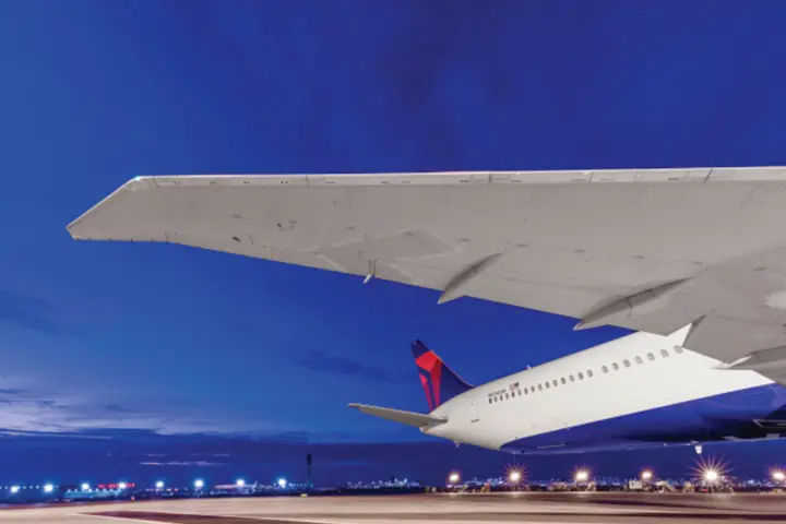 Overlooking an evening skyline lit by the runway, Delta's Boeing 767-400 dorsal area features a wingspan of 171 feet and a tail height of over 50 inches.