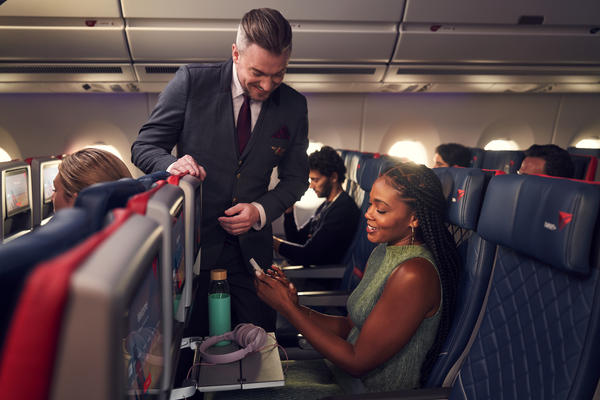 A Delta Flight Attendant assists a customer seated in Delta Comfort+ with their mobile device.