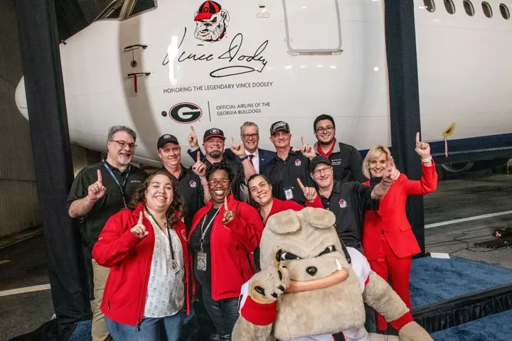 Delta leaders and UGA alum stand in front of a Boeing 767-400 featuring a memorial seal honoring renowned UGA football couch Vince Dooley.