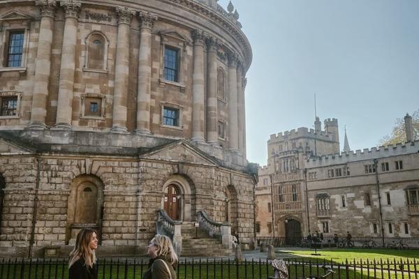 Two people stand in front of the Radcliffe Camera building at the University of Oxford.