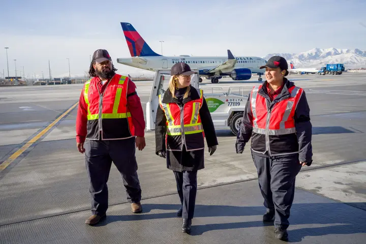 Delta Chief Sustainability Officer Pam Fletcher (middle) talks with Aircraft Load Agent Thomas Tuikolovatu (left) and Ramp Agent Sinai Pauni (right) about how they use eGSE at Salt Lake City International Airport (SLC).