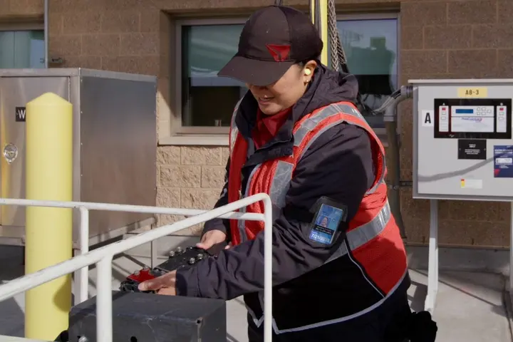 Delta Ramp Agent Sinai Pauni (left) plugs in an electric bag tractor for charging at Salt Lake City International Airport (SLC).