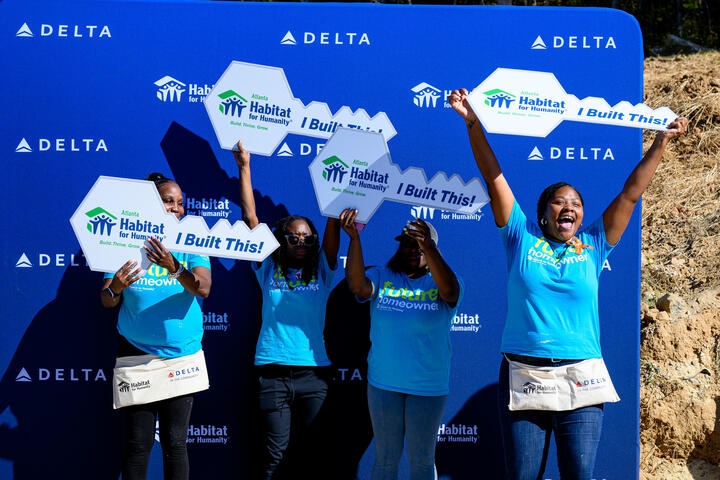 Habitat for Humanity homeowners pose for a photo cheering and holding large key-shaped cutouts.