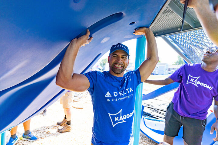 Delta employee volunteer smiling as he holds up a blue playground piece at a Kaboom build