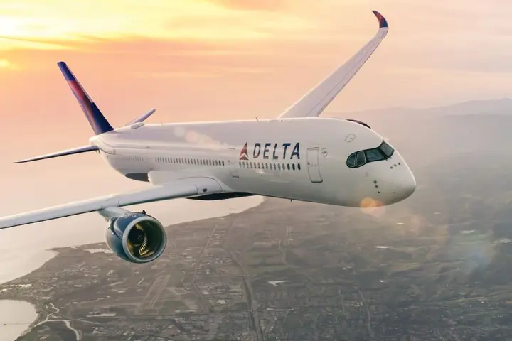 Delta aircraft flying above a coastal city with sun setting in background