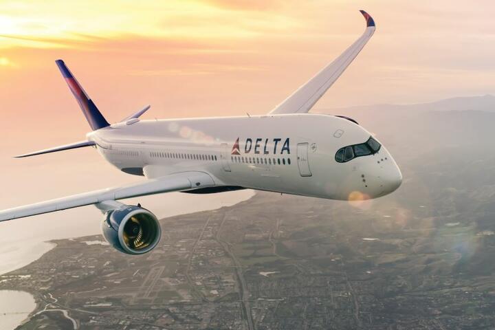 Delta aircraft flying above a coastal city with sun setting in background