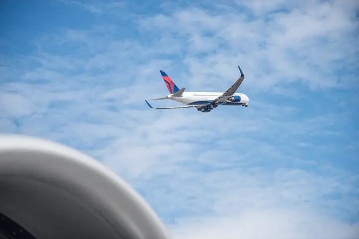 Delta 767 aircraft shortly after takeoff with blue sky and clouds in background
