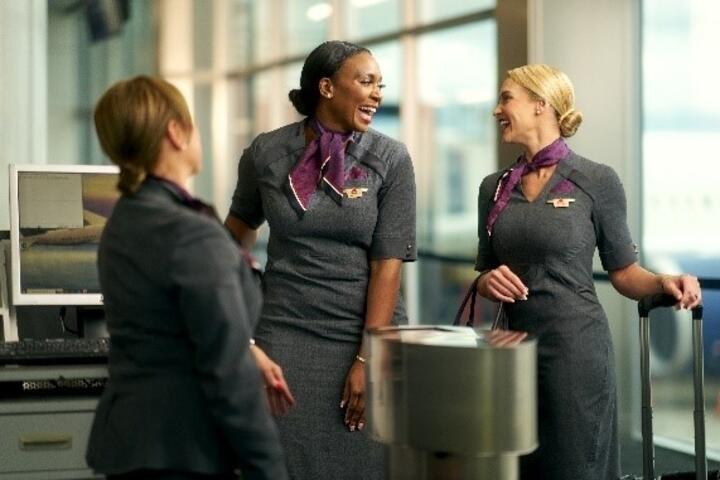 Three Delta flight attendants standing together, laughing with one another.