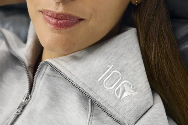 Woman wearing light grey Spanx half zip embroidered with Delta Centennial logo. 