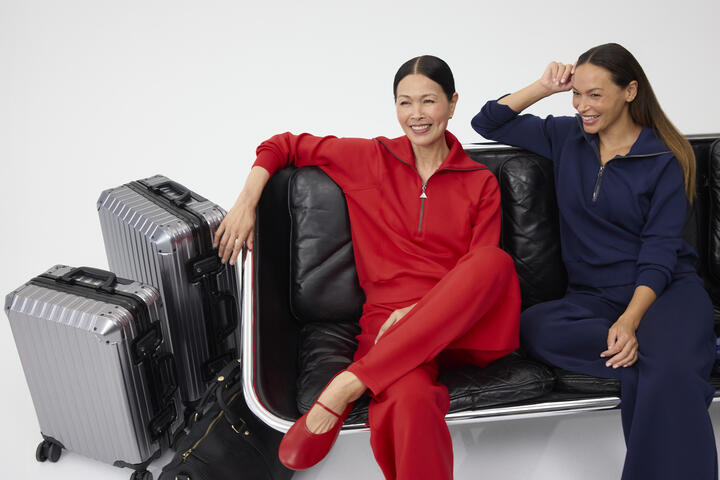 Two smiling women, sitting next to each other dressed in red and navy Spanx outfits.