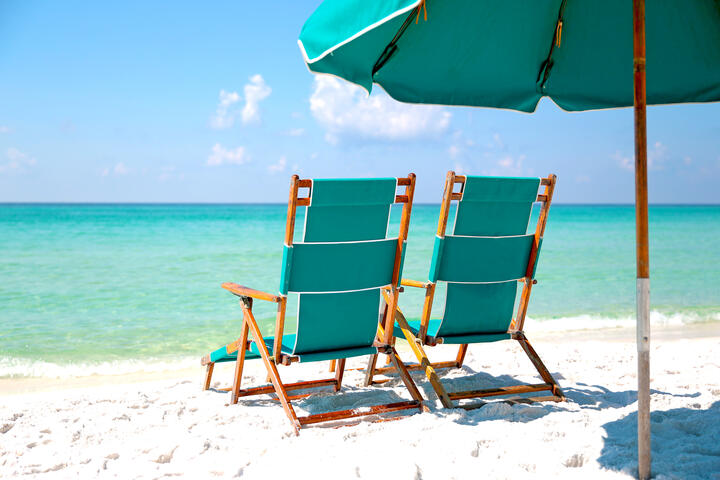 Two empty beach chairs in the sand facing turquoise blue ocean.