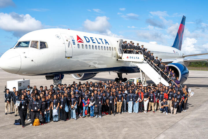 Group shot of DREAM flight attendees standing in front of Delta plane on tarmac. 