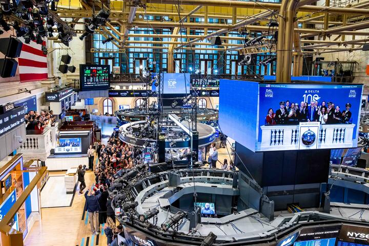 Overhead shot of NYSE floor with main screen displaying Ed and Delta people ringing the bell.