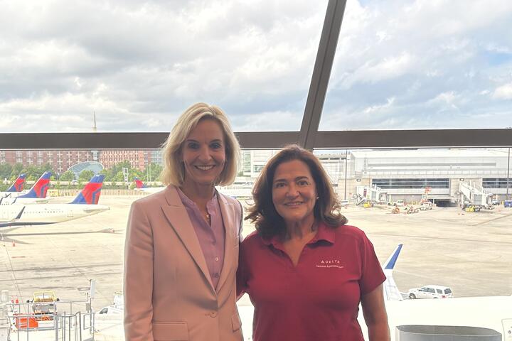 Delta employees Allison Ausband and Nancy Cohn posing against a backdrop of the Boston airport ramp.