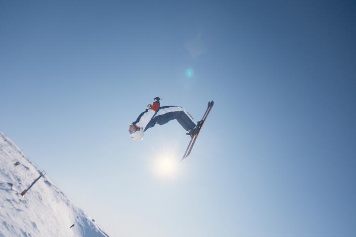 A skier performs a high aerial trick against a clear blue sky on a snowy mountain slope