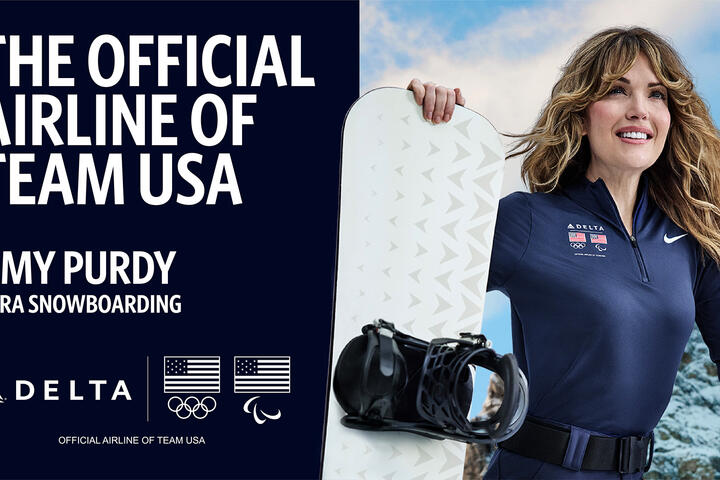 Promotional graphic with text reading ‘The Official Airline of Team USA’ and ‘Amy Purdy – Para Snowboarding,’ along with Delta, Olympic and Paralympic logos. On the right, athlete in navy jacket holds a snowboard against a snowy mountain backdrop