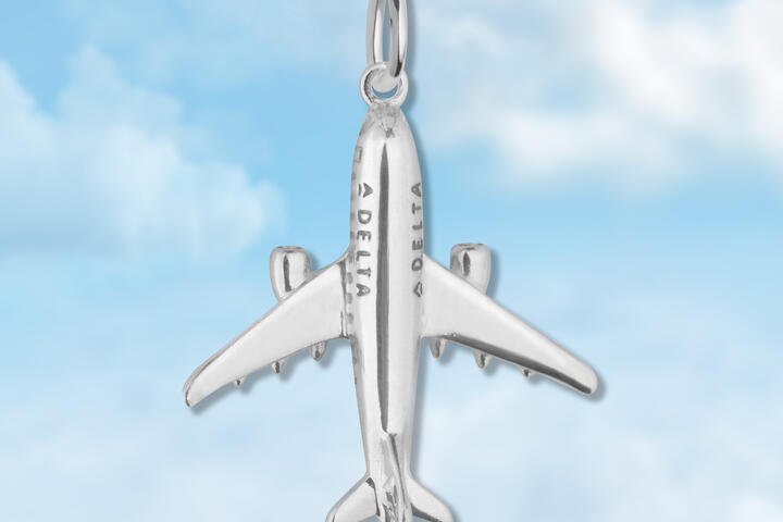 Silver plane charm on blue cloud background. 