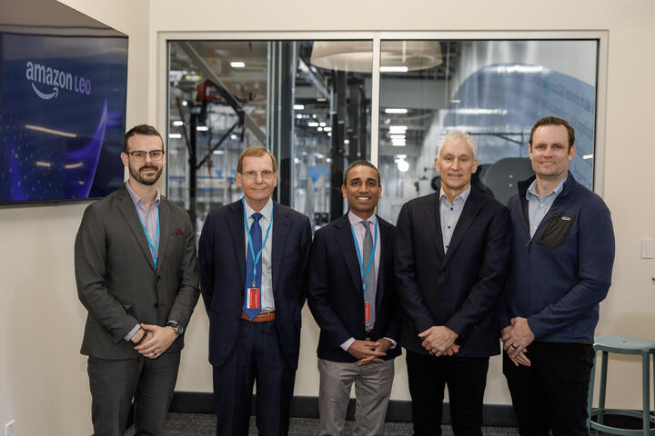 Members of Delta and Amazon Leo teams pose for a picture with factory as backdrop.