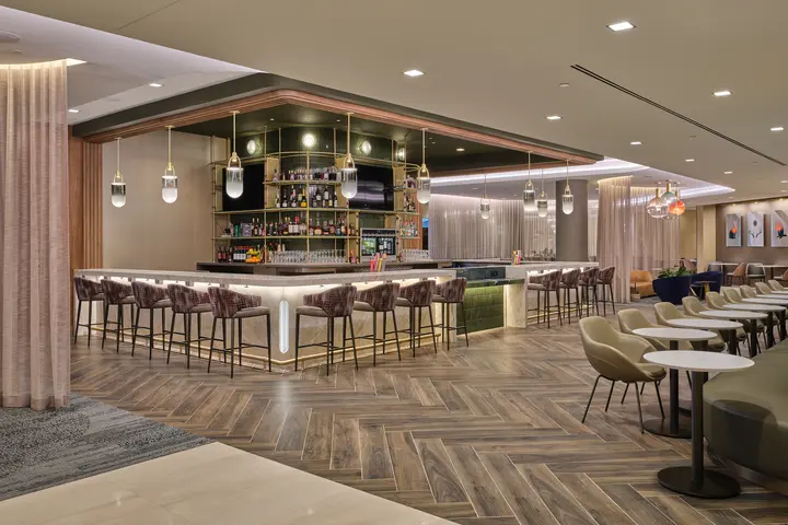 Lounge bar with high‑back stools, illuminated shelving, warm lighting and adjacent seating areas with small tables