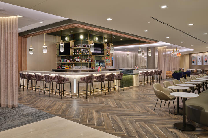 Lounge bar with high‑back stools, illuminated shelving, warm lighting and adjacent seating areas with small tables