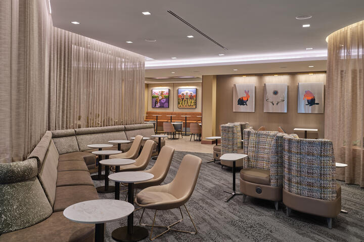 Central lounge area with cushioned seating, small round tables, soft divider curtains and colorful artwork on the walls