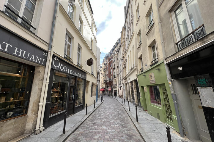 Narrow cobblestone street lined with small boutiques and pastel buildings in a historic Paris neighborhood.