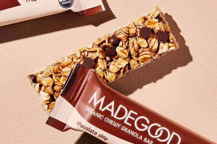 An unpackaged MadeGood® Chocolate Chip Chewy Granola Bar sits under a packaged granola bar