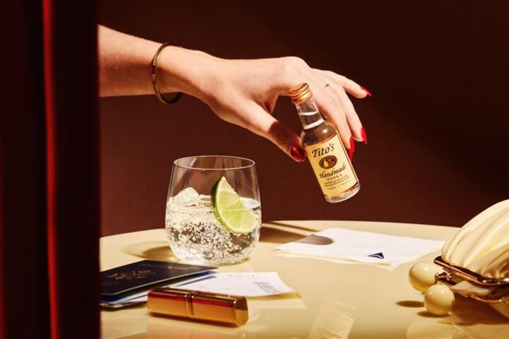 A hand holds an airplane bottle of Tito's Vodka