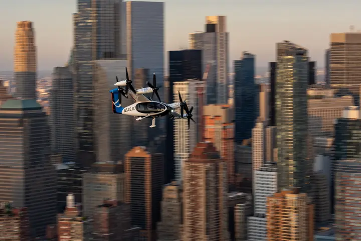 Joby Electric air taxi flying above midtown Manhattan with blurry city skyline in the background.