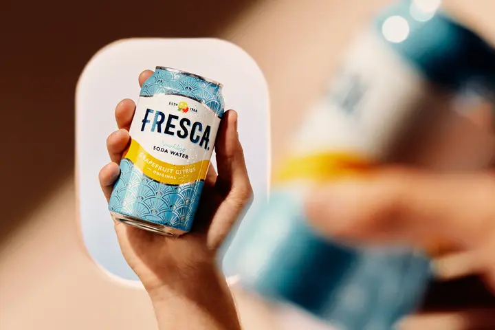 Hand holding a chilled Fresca grapefruit citrus soda can, with an airplane window softly blurred in the background.