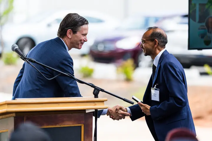 Two individuals exchange a handshake near a podium and microphone at an event