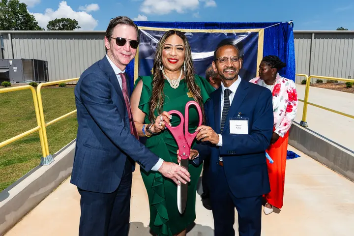 Group of individuals holding oversized ceremonial scissors at an outdoor ribbon-cutting event.