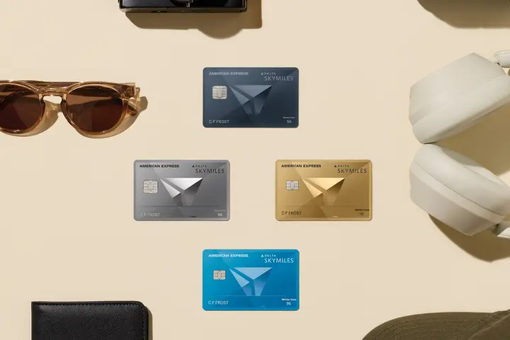 Flat lay of Delta SkyMiles American Express Cards surrounded by travel essentials, including a passport, camera, sunglasses, headphones, and luggage accessories.