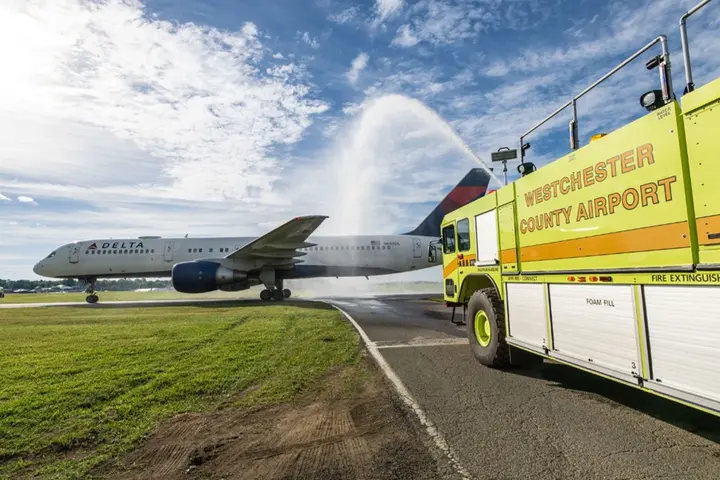 Delta airplane receives water salute from airport fire truck on runway.