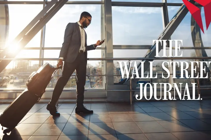 Traveler in a suit walks through a sunlit airport terminal, pulling a rolling suitcase and looking at a phone, with “The Wall Street Journal” text overlaid.