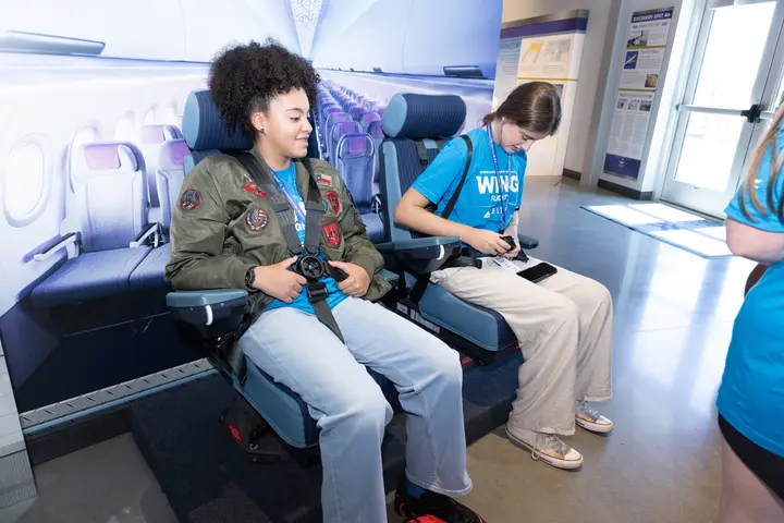 Students test aircraft passenger seats and seatbelt equipment during a hands-on aviation learning experience.