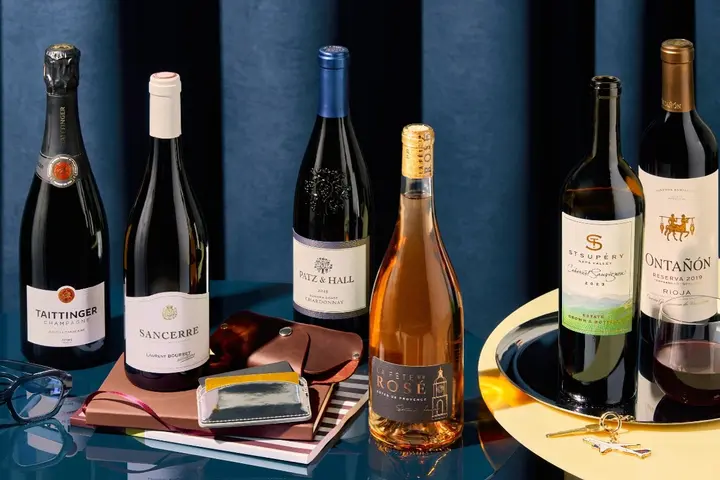 Assortment of wine bottles arranged with travel accessories, a glass of wine and decorative props.