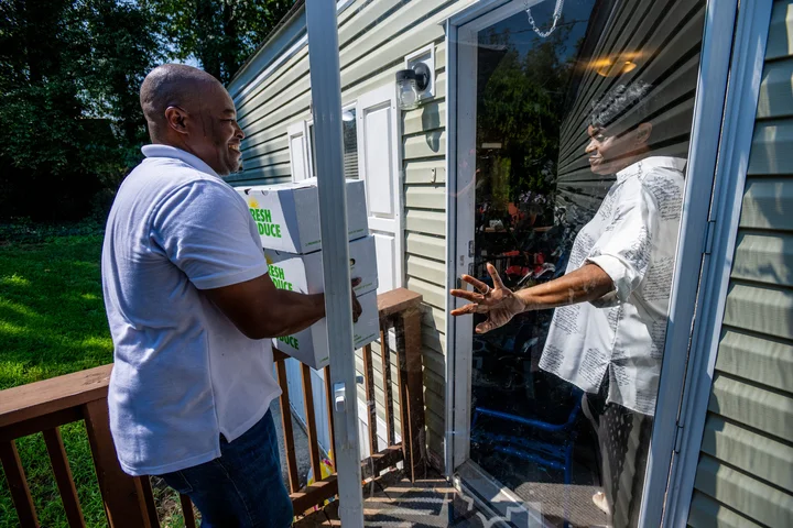 An Online Food Pantry volunteer delivers boxes of fresh produce to a resident at a home entrance.