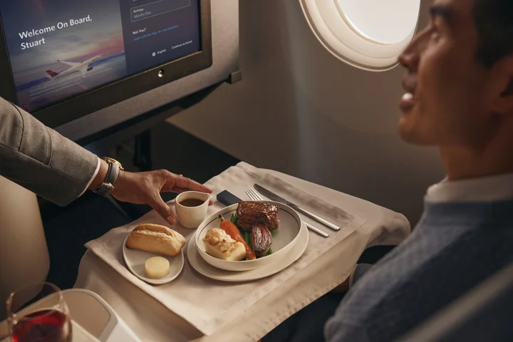 Flight attendant serves a plated meal with bread and vegetables to a passenger in a Delta One cabin.