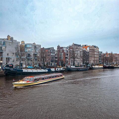 A canal boat travels along a river lined with traditional narrow buildings and moored houseboats.