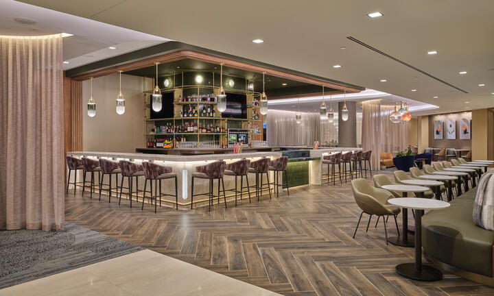 Lounge bar with high‑back stools, illuminated shelving, warm lighting and adjacent seating areas with small tables