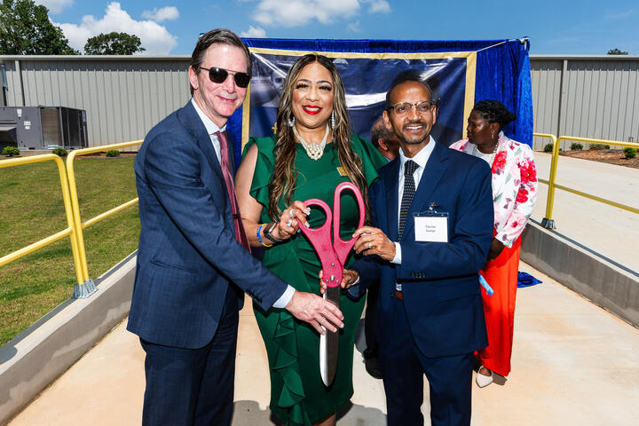 Group of individuals holding oversized ceremonial scissors at an outdoor ribbon-cutting event.