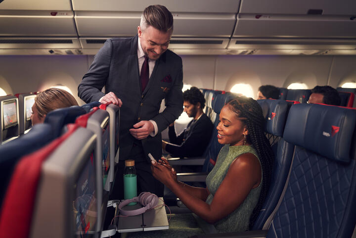 A Delta Flight Attendant assists a customer seated in Delta Comfort+ with their mobile device.