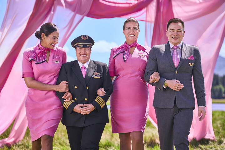 Four Delta employees in pink uniforms walking arm in arm