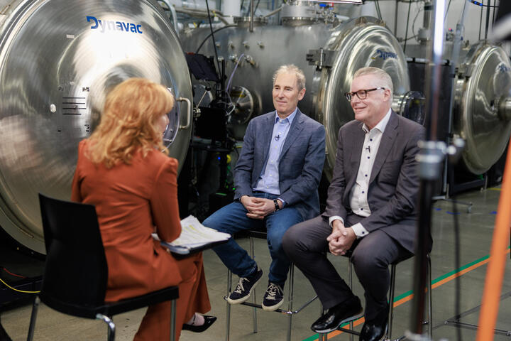 Ed Bastian and Andy Jassy sitting down during media interview with Amazon Leo factory in background.