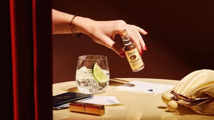 A hand holds an airplane bottle of Tito's Vodka
